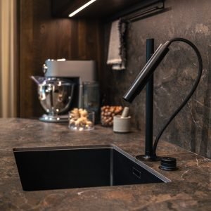 A wide angle shot of a modern kitchen area with dark marble and an elegant black sink.